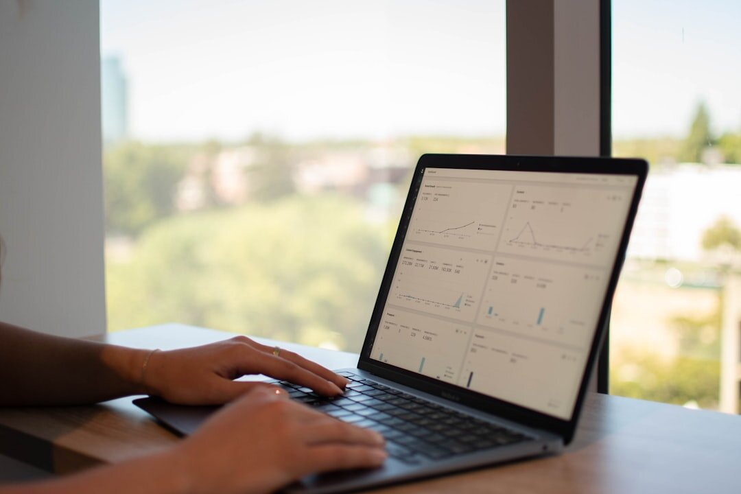 Close-up of hands typing on a laptop keyboard with charts visible on the screen